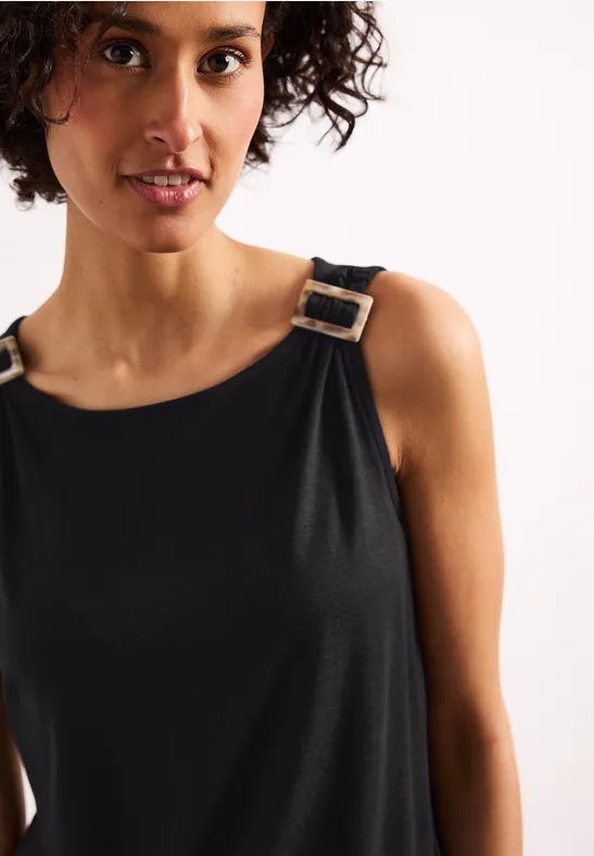 Close-up van persoon in een mouwloze zwarte top met zilverkleurige gespen op de schouderbanden.