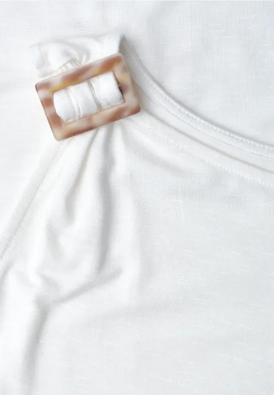 Close-up van een witte top met een vierkante, hoornkleurige gesp aan het bandje.