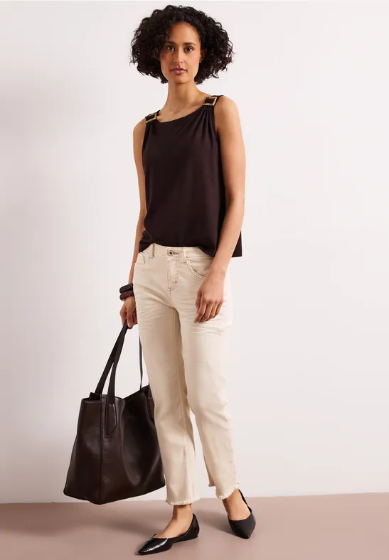 Personne en top noir sans manches, pantalon beige et ballerines noires, tenant un sac en cuir noir.