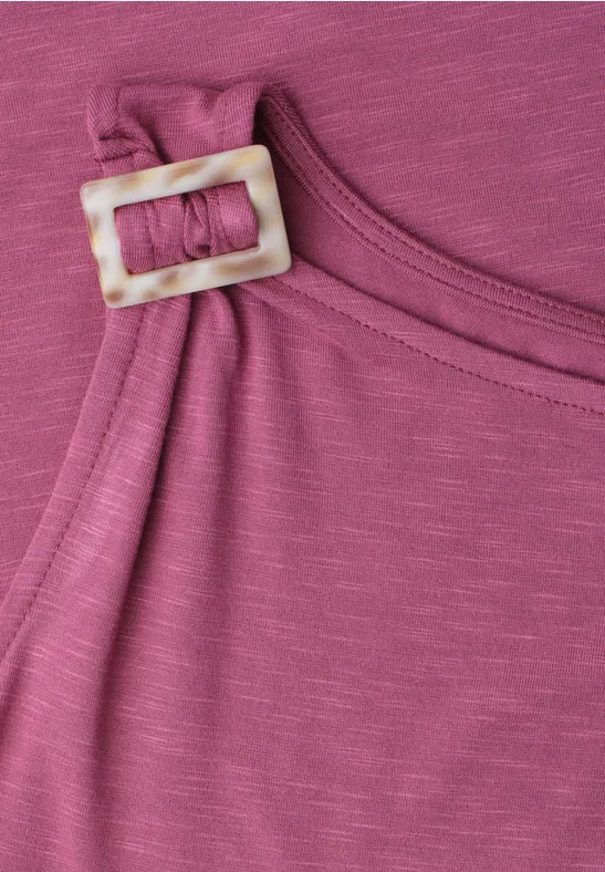 Close-up van een roze top met brede schouderband en vierkante, parelmoeren gesp.