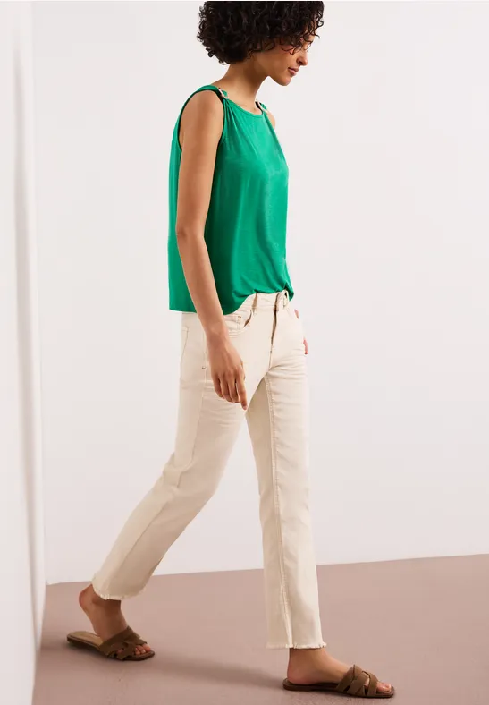 Vrouw in groen topje, beige broek en sandalen, lopend opzij.