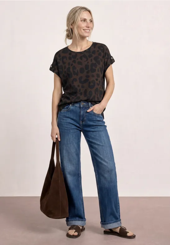 Vrouw in casual outfit: zwart shirt met patroon, wijde jeans, sandalen en grote bruine tas.