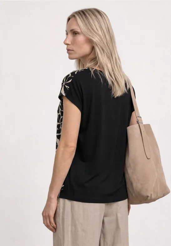 Blonde vrouw van achteren in zwarte T-shirt en beige broek, met grote beige draagtas.