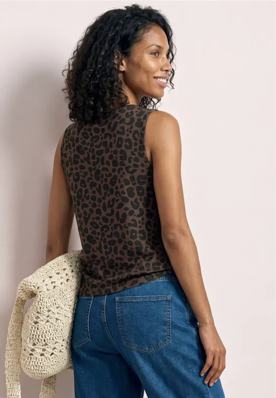 Eine Frau mit lockigem Haar trägt ein ärmelloses Leopardenmuster-Top, blaue Jeans und hält eine gehäkelte Tasche.