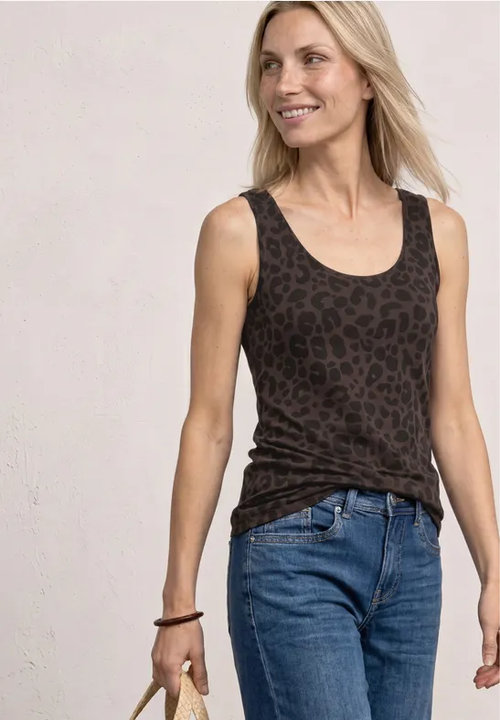 Vrouw in spijkerbroek en donker luipaardprint top voor een lichte achtergrond.