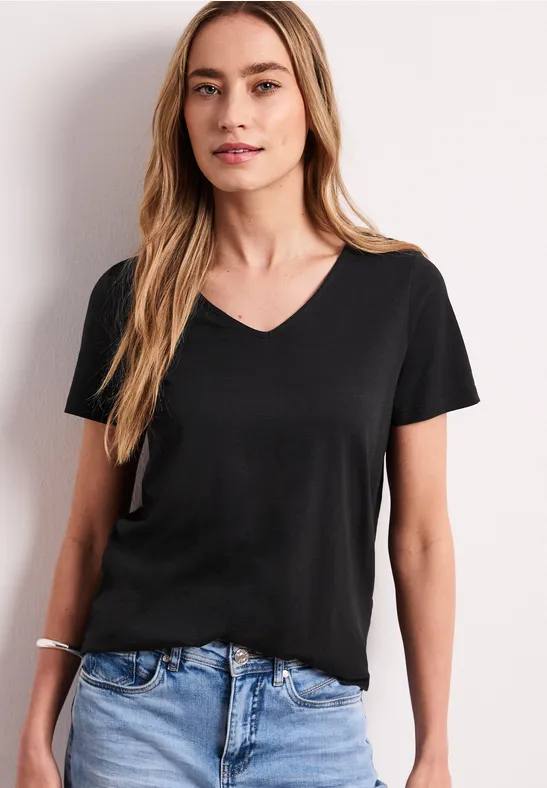 Vrouw met zwart V-hals t-shirt en blauwe jeans voor een witte achtergrond.