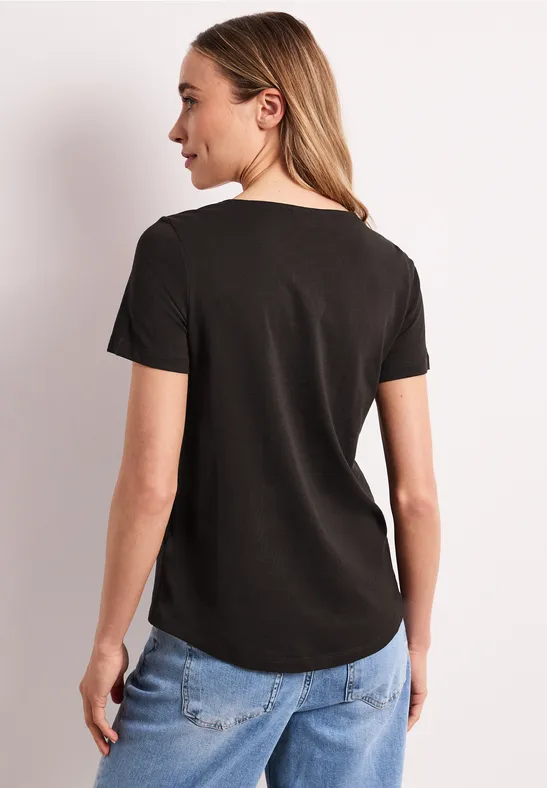 Femme vue de dos portant un t-shirt noir et un jean bleu sur fond clair.