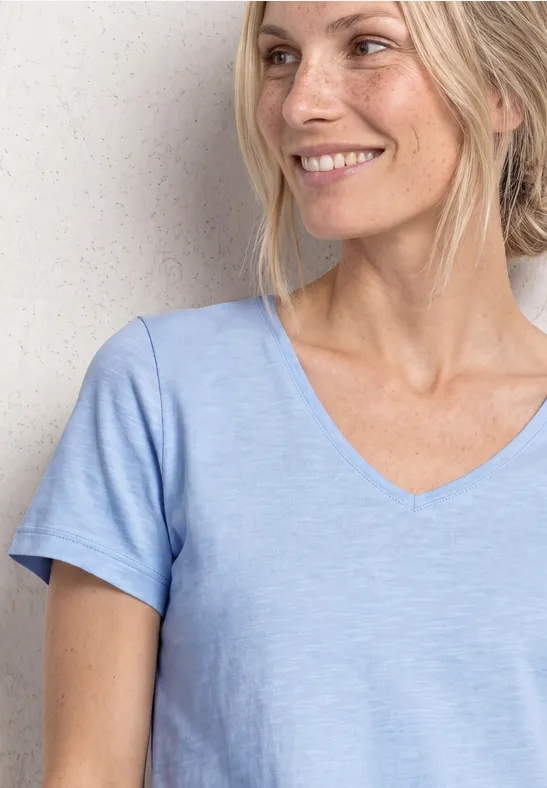 Frau in hellem, kurzärmligem V-Shirt steht vor heller Wand