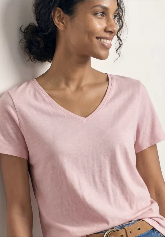 Frau in rosa V-Ausschnitt-T-Shirt vor neutralem Hintergrund, Gesicht unscharf, von Hüfte bis Hals sichtbar.