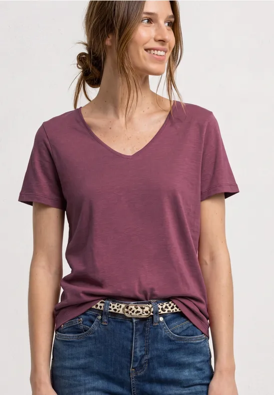 Vrouw in bordeaux T-shirt met V-hals en jeans met luipaardriem, haar in een knot.