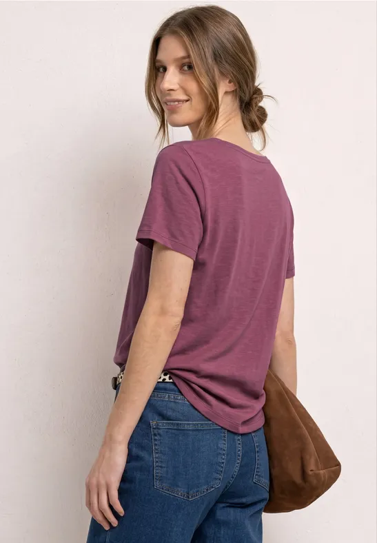 Vrouw van achteren met paars T-shirt, spijkerbroek en bruine schoudertas.