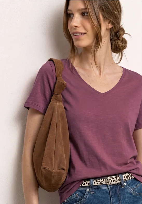 Vrouw met opgestoken haar, paarse V-hals T-shirt, luipaardriem en bruine schoudertas voor lichte achtergrond.