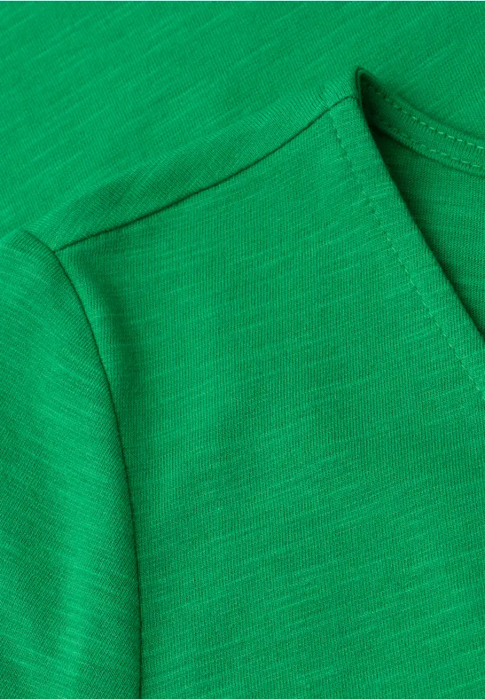 Close-up van een groen T-shirt met zichtbare schoudernaden en ronde halslijn.