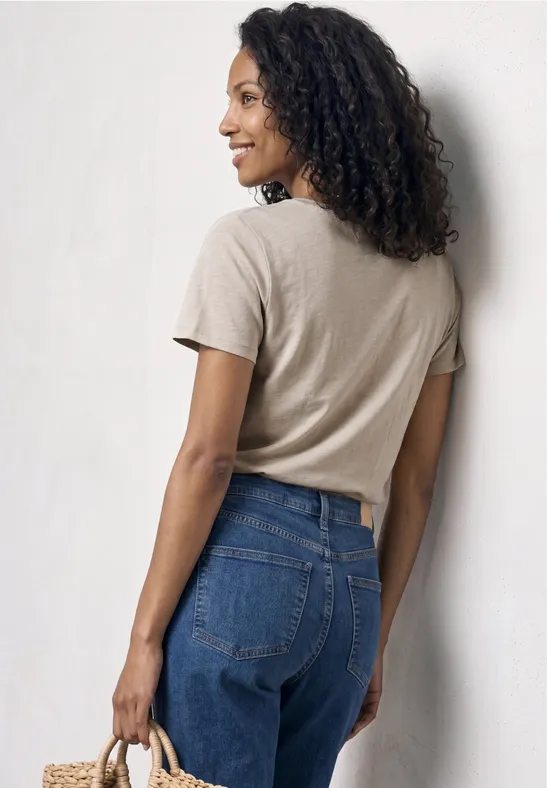 Frau von hinten in beigefarbenem T-Shirt, blauen Jeans und Strohtasche in der Hand.