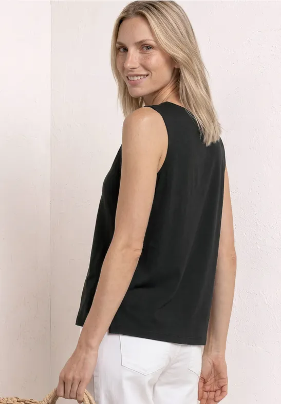 Persoon in zwart mouwloos topje en witte broek, zijwaarts gedraaid.