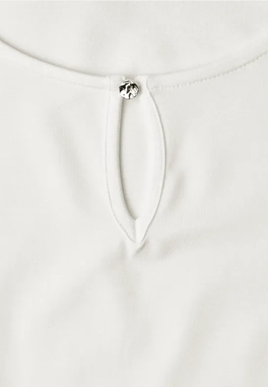 Witte top met ronde hals, druppelvormige opening en klein metalen sluitinkje.