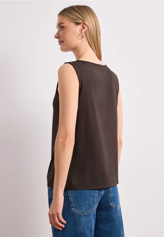 Vrouw van achteren in zwarte mouwloze top en blauwe jeans voor een lichte achtergrond.