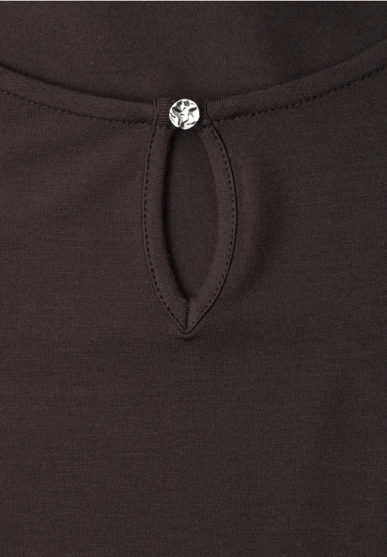 Close-up van een donker shirt met een druppelvormige uitsnijding bij de hals, versierd met een kleine, glinsterende knoop.