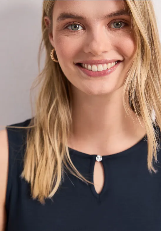 Glimlachende blonde vrouw in donkerblauw topje met druppelnek en decoratieve knoop