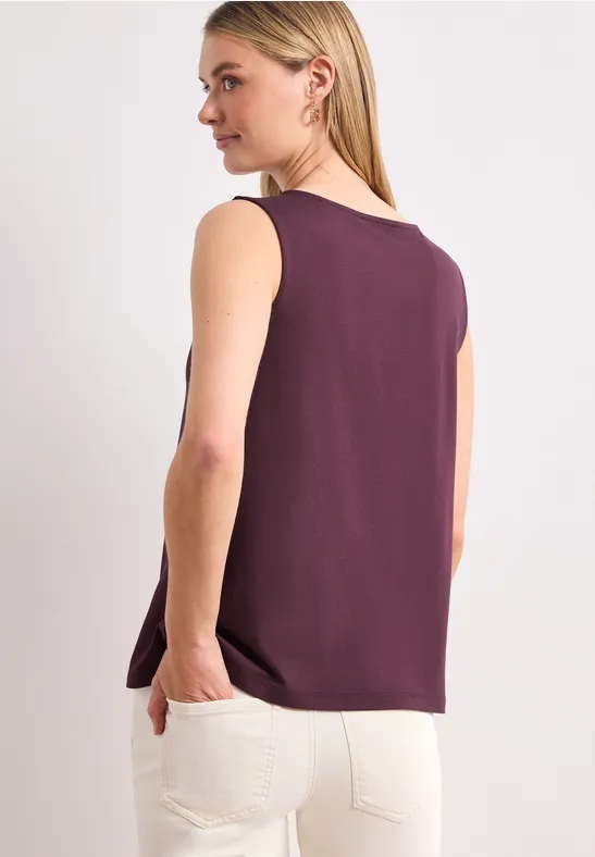 Vrouw van achter gefotografeerd met een mouwloze bordeaux top en een witte broek.