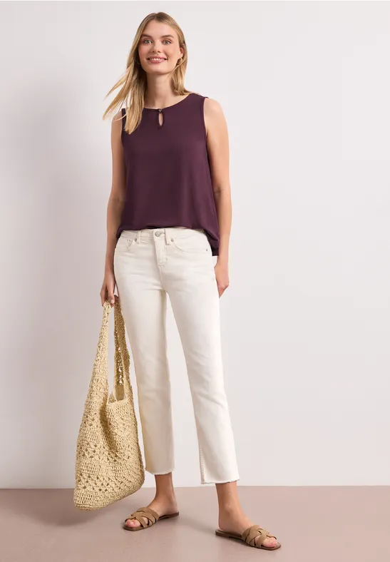 Vrouw in paarse top, witte culottes, sandalen en grote gevlochten strandtas.