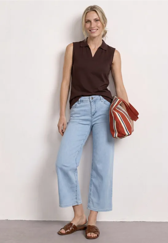 Vrouw in donkerbruin mouwloos topje, lichtblauwe wijde jeans, bruine sandalen en gestreepte tas.