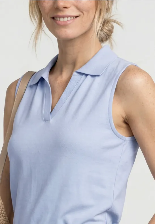 Close-up van een glimlachende vrouw in lichtblauw mouwloos poloshirt, schouders en borst zichtbaar.
