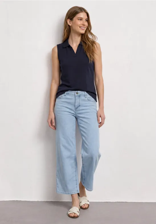 Frau im ärmellosen schwarzen Top und hellblauen weiten Jeans mit Sandalen.