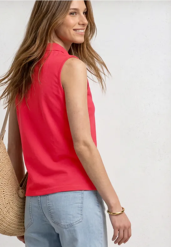 Portrait de profil d'une femme en débardeur rouge, jean clair et sac en paille sur fond blanc.