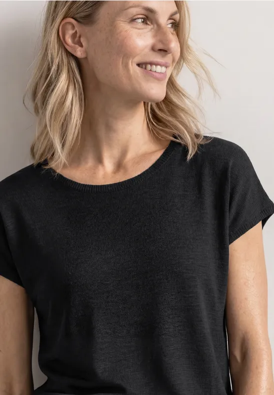 Close-up van een vrouw vanaf borsthoogte in een effen zwart T-shirt, halflang blond haar.
