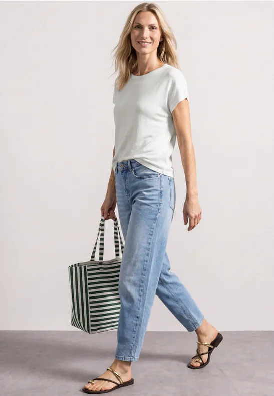 Femme en t-shirt blanc, jean bleu et sandales porte un sac rayé en marchant.