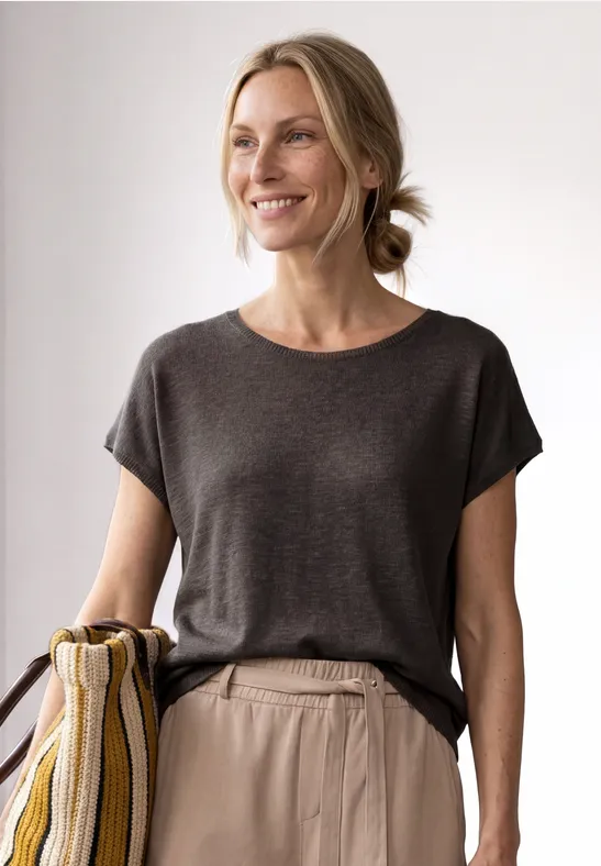 Femme portant un t-shirt gris foncé et un sac rayé sur l’épaule, cheveux noués en chignon décontracté.