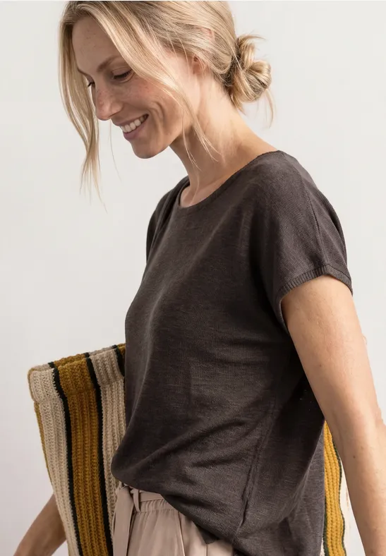 Femme portant un t-shirt marron foncé et un pantalon beige décontracté sur fond clair.