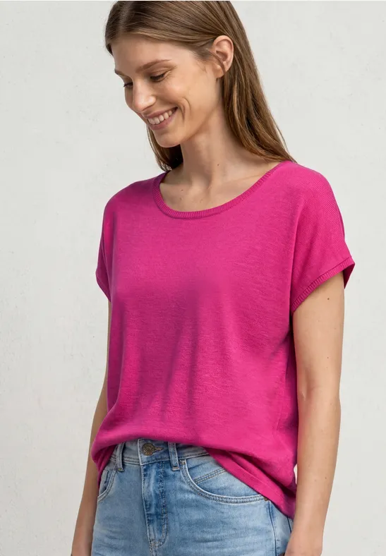 Vrouw in roze T-shirt en blauwe jeans voor neutrale achtergrond.