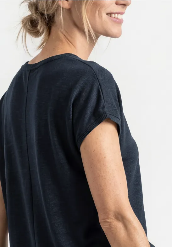 Frau im Profil trägt dunkelblaues kurzärmeliges Shirt und lächelt leicht.