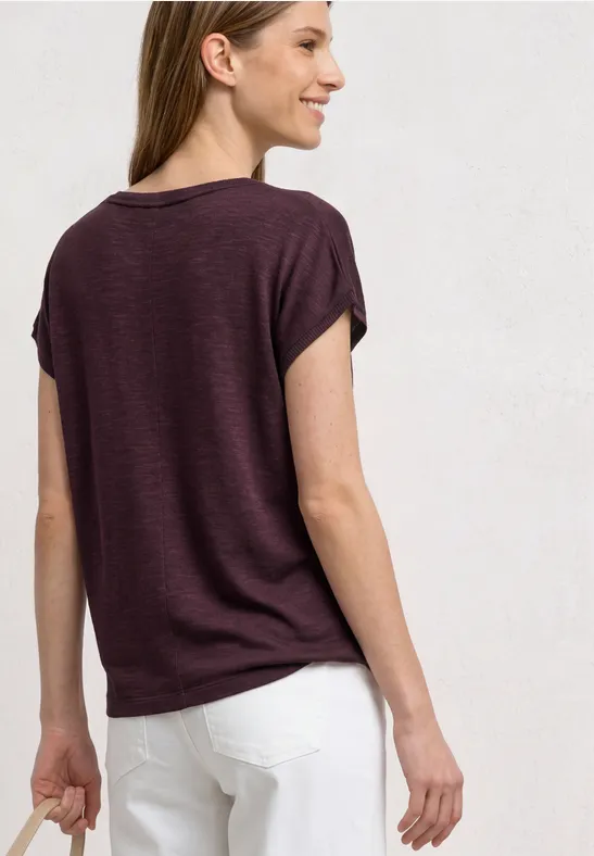 Frau trägt violettes T-Shirt und weiße Hose, von hinten fotografiert.