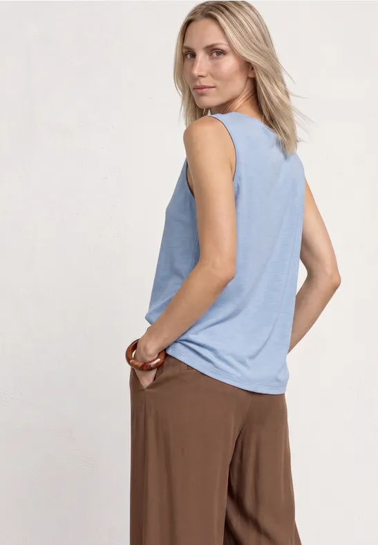 Eine Person in ärmellosem hellblauem Top und brauner Hose, seitlich stehend.