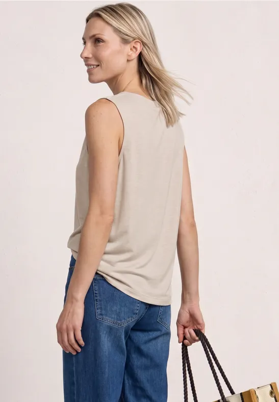 Frau von hinten in beige ärmellosem Oberteil, blauen Jeans und mit einer Handtasche in der rechten Hand