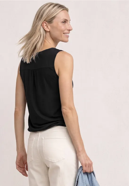 Eine Frau von hinten in schwarzem Top und weißen Hosen hält eine Tasche.