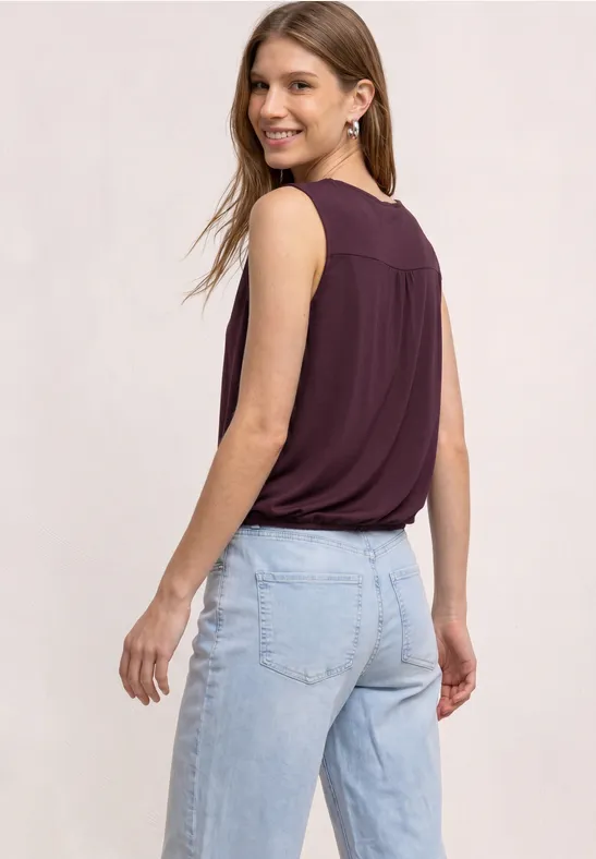 Rückansicht einer Frau in einem ärmellosen lila Top und hellblauer Jeans.