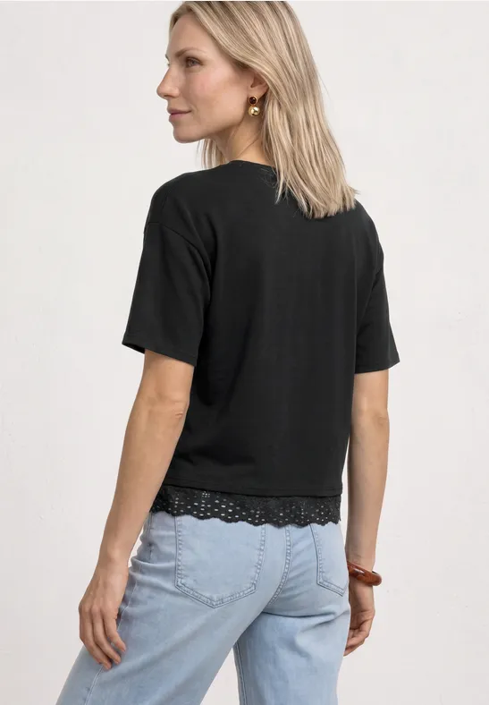 Vrouw van achteren met halflang blond haar, zwart t-shirt met kantzoom en lichtblauwe jeans
