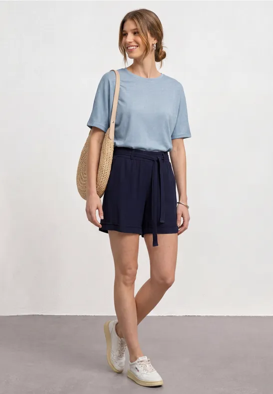Vrouw met blauw t-shirt, donkerblauwe short, strozak en witte sneakers.