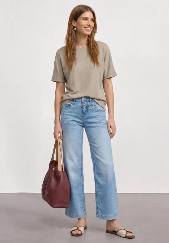 Vrouw met grijs T-shirt, lichtblauwe jeans, zwarte sandalen en een bordeaux handtas.