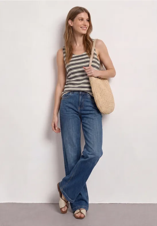 Een vrouw draagt een gestreept topje, wijde jeans en een rieten tas.