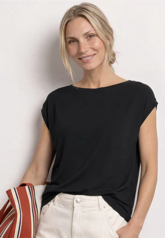 Eine Frau trägt ein schwarzes, locker sitzendes T-Shirt mit hochgekrempelten Ärmeln und weiße Hosen.