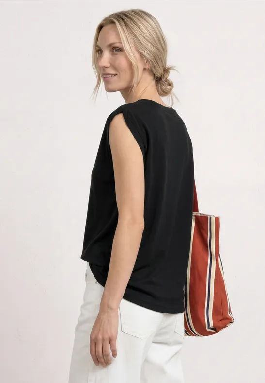 Frau von hinten in schwarzem Top, weißer Hose und blondem Dutt, mit gestreifter Tasche.