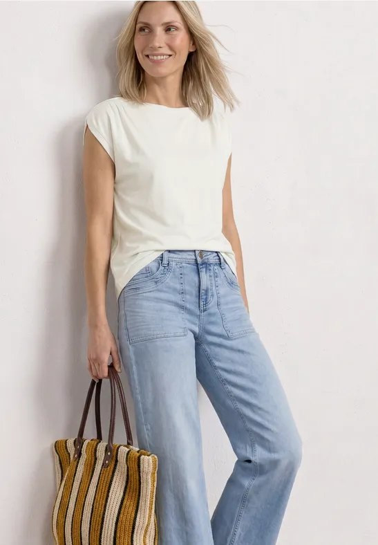 Vrouw in witte t-shirt, lichtblauwe jeans en gestreepte tas voor een witte achtergrond.