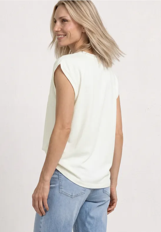 Vrouw van achteren in een wit mouwloos shirt en lichtblauwe jeans, kijkend over haar schouder.