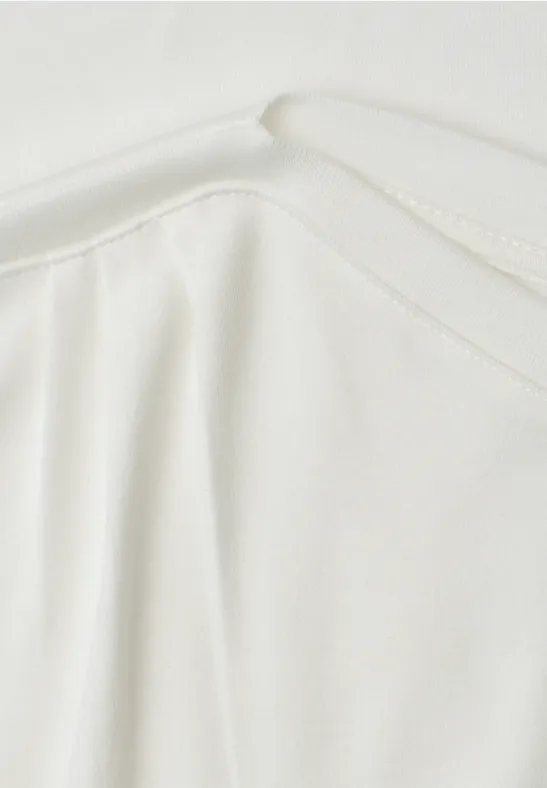 Close-up van een wit kledingstuk met ronde hals en subtiele plooien