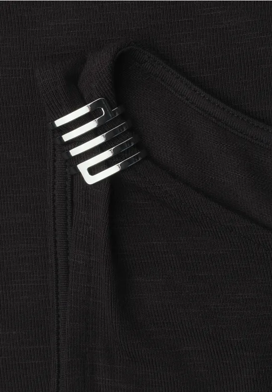 Close-up van zwarte stof met een zilverkleurige gesp op de schouder, detail van een top.